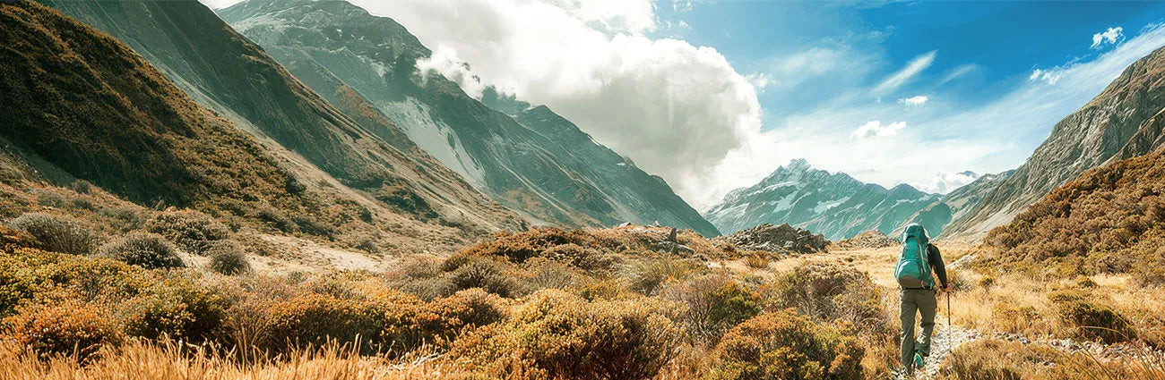 Backpacker hiking through a scenic mountain valley under blue skies and dramatic clouds | Altitude Philippines