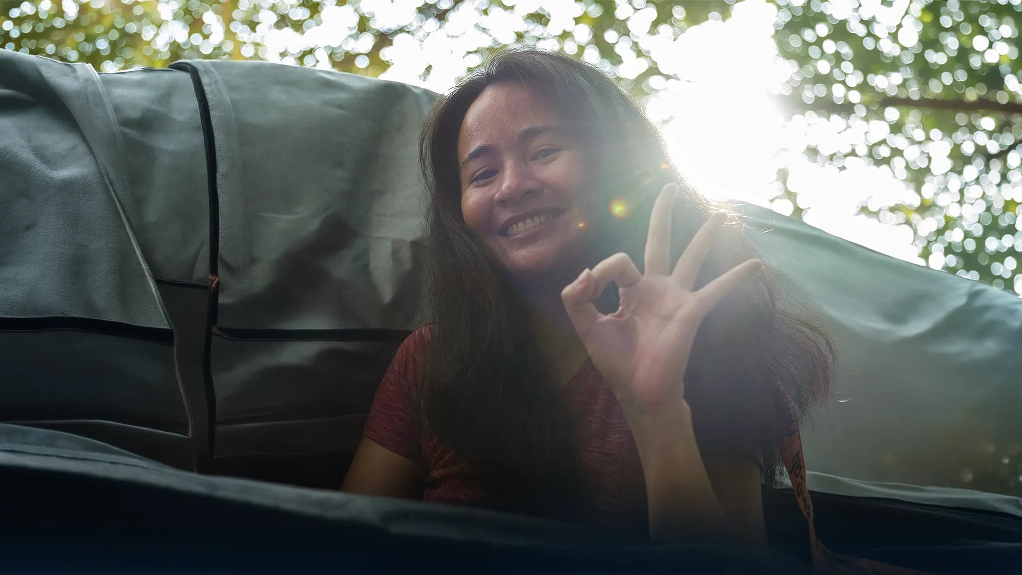 Woman smiling beside camping gear while making an OK hand gesture outdoors | Altitude Philippines
