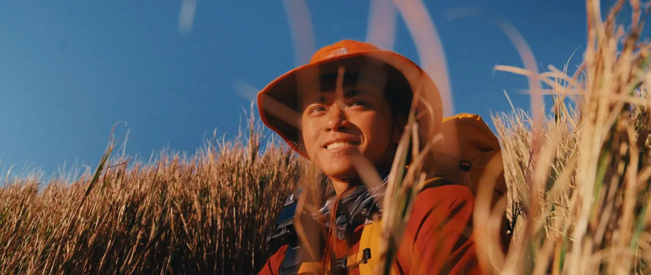 Hiker with a backpack enjoying a scenic grassland trail under clear skies | Altitude Philippines